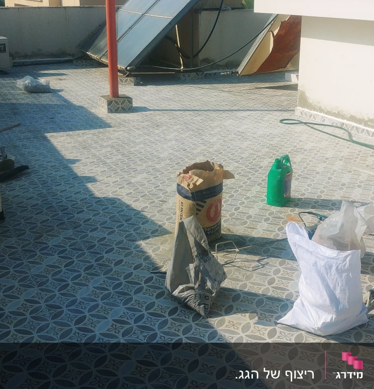 שק מלט, כלי עבודה וצינור על רצפה מרוצפת